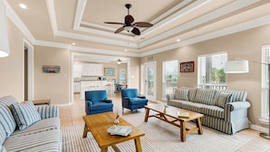 A spacious living room with a large sofa, two armchairs, a coffee table, and a ceiling fan.