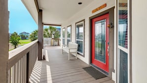 A covered porch with a red door, a white bench, and a view of a green landscape.