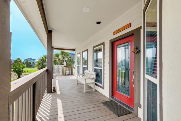 A covered porch with a red door, a white bench, and a view of a green landscape.