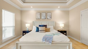 A bedroom with a large bed, two bedside tables, a window with blinds, and three wall-mounted pictures.