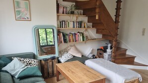A cozy living room with a green sofa, a wooden table, a bookshelf, and a staircase.