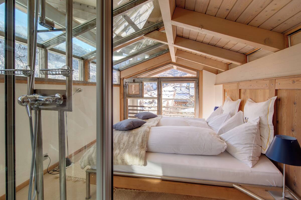 A bedroom with a bed, pillows, a lamp, and a shower area with a glass door.