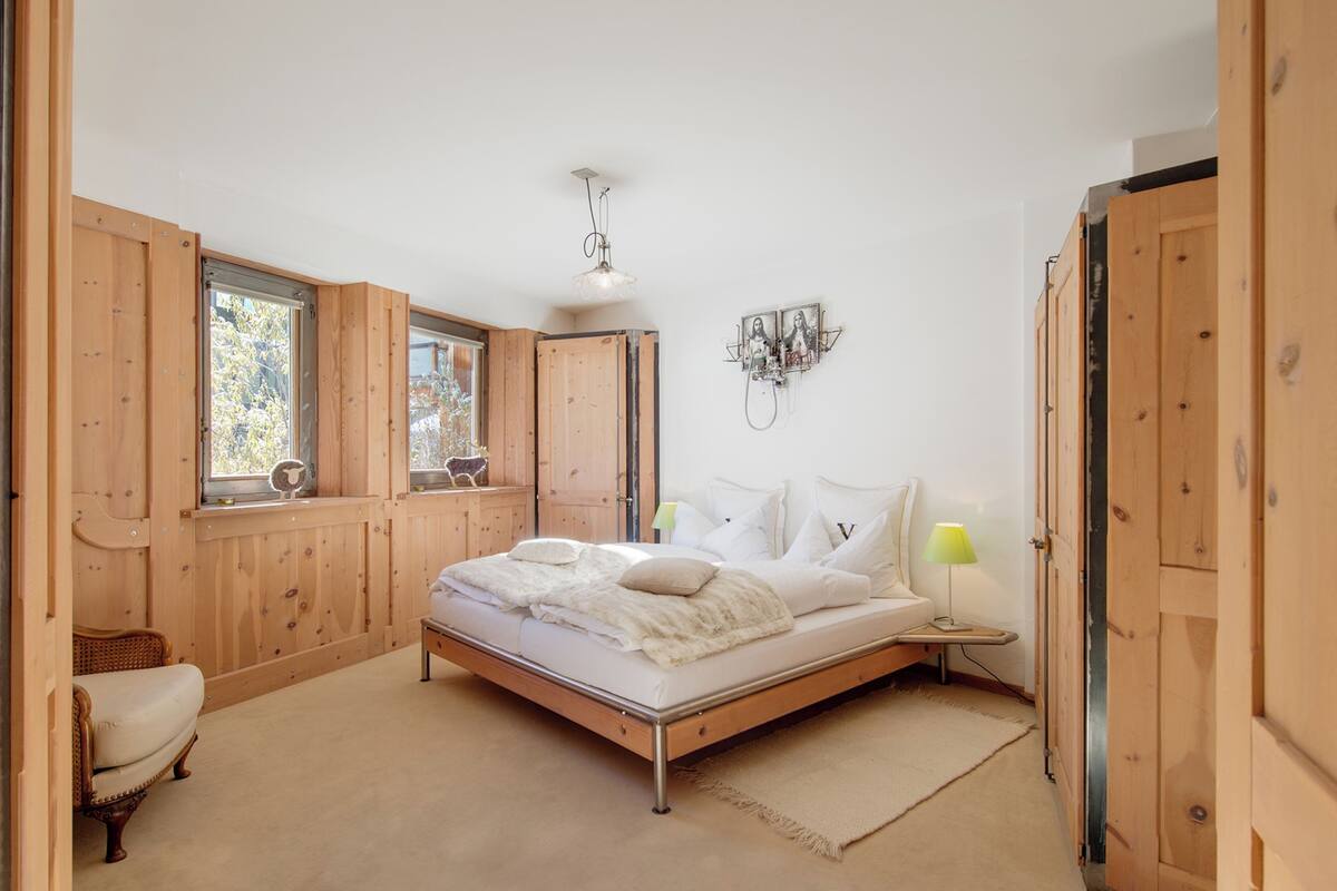 A bedroom with a bed, wooden wardrobe, and a window with a view of trees.
