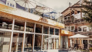 A modern building with large glass windows, a pool, and outdoor seating. - Backstage Hotel Serviced Apartments (Zermatt)