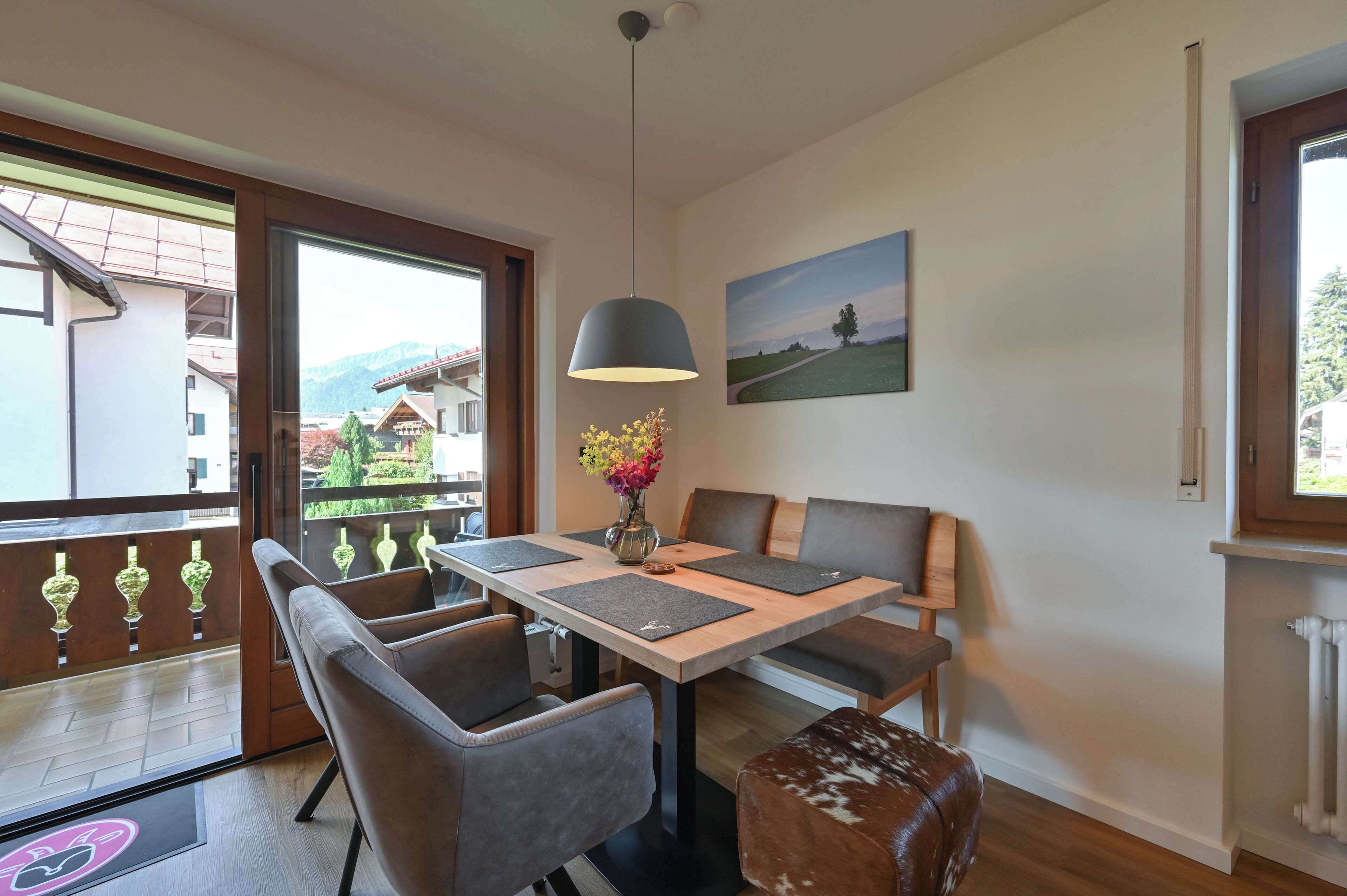 A dining area with a table, chairs, a vase with flowers, and a painting on the wall.