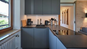 Een moderne keuken met grijze kastjes, een zwart aanrechtblad en een raam met uitzicht op de omgeving.