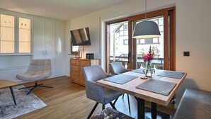 Een moderne eetruimte met een houten tafel, grijs beklede stoelen en een groot raam met uitzicht op gebouwen.