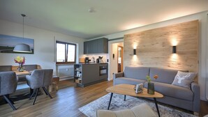 Een moderne woonkamer met een grijze bank, een houten salontafel en een eetgedeelte met grijze stoelen.