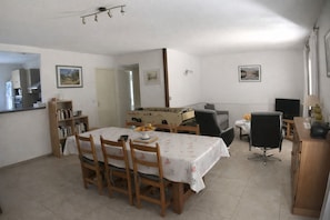 A dining area with a table, chairs, a bookshelf, a foosball table, and a television. - Havre de Paix Pour Moments en Famille ou Entre Amis à 10 Min. D'uzès (Baron)
