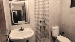 A bathroom with a pedestal sink, a toilet, and a shower with a tiled wall. - Hotel Shri Ram By GRB (New Delhi)