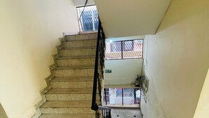 A staircase with a metal railing, leading to a landing with a window and an 'EXIT' sign. - Hotel Shri Ram By GRB (New Delhi)