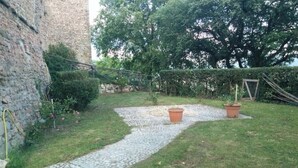 A paved garden path leading to a grassy area with two potted plants and a hedge.