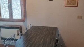 A room with a wooden dining table, a metal chair, a radiator, and a window with a view of a stone wall.