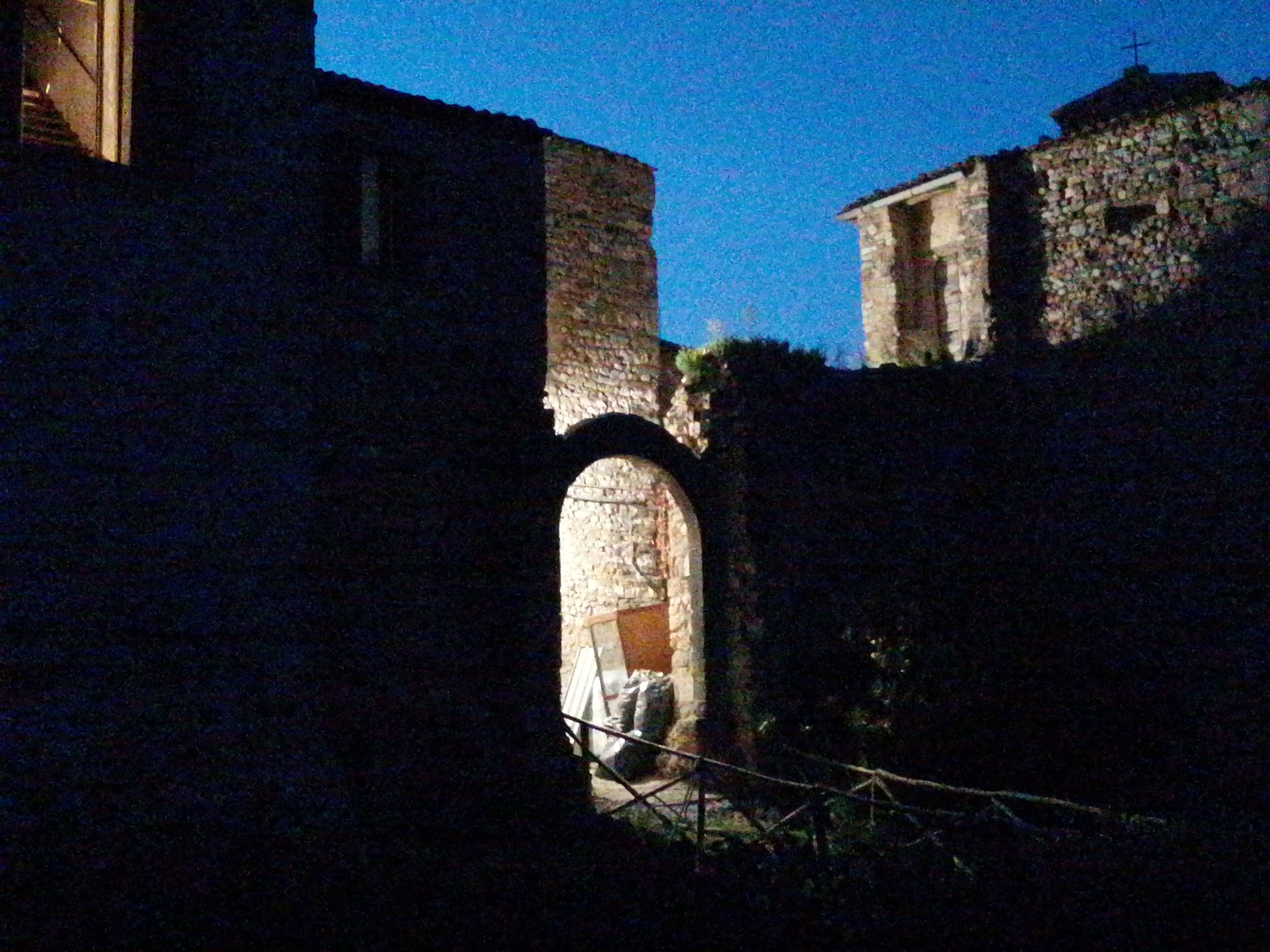 Ein rundbogiges Steintor, das zu einem Gebäude mit Kruzifix führt, was auf eine religiöse oder historische Stätte hindeutet.