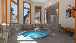 A hot tub with metal ladders, surrounded by stone walls and large windows. - Peak 9 Breck Condo w/Hot Tub & Mountain Views (Breckenridge)