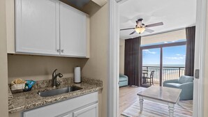 A kitchen with a granite countertop, stainless steel sink, and white cabinets. There is a balcony with a view of the ocean and a ceiling fan. - Beachfront Serenity 1 Bedroom 2 Bathroom Escape (North Myrtle Beach)