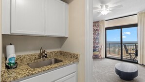 Eine Küche mit Granitabdeckung, weißen Schränken und einer Spüle. Es gibt einen Balkon mit Meerblick und einen Deckenventilator.