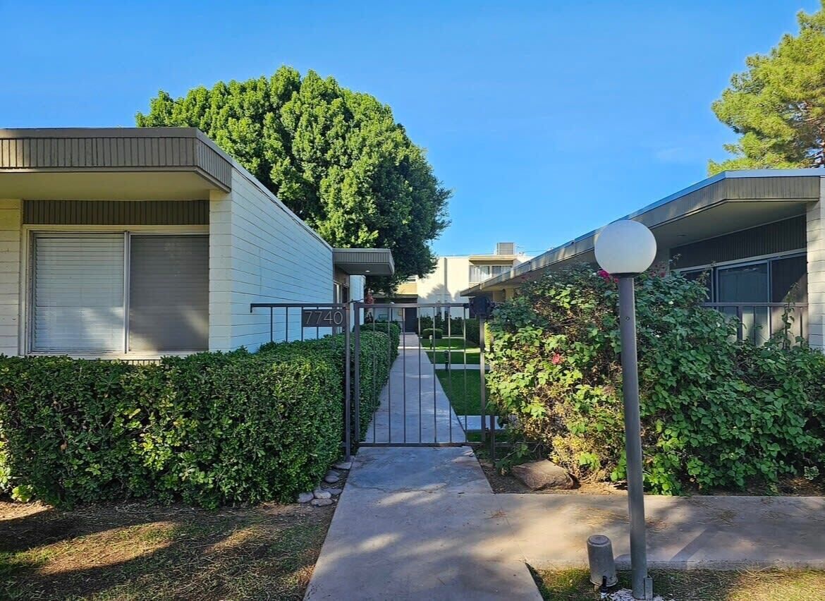 Un sendero conduce a la entrada porticada de un complejo residencial bajo un cielo despejado.