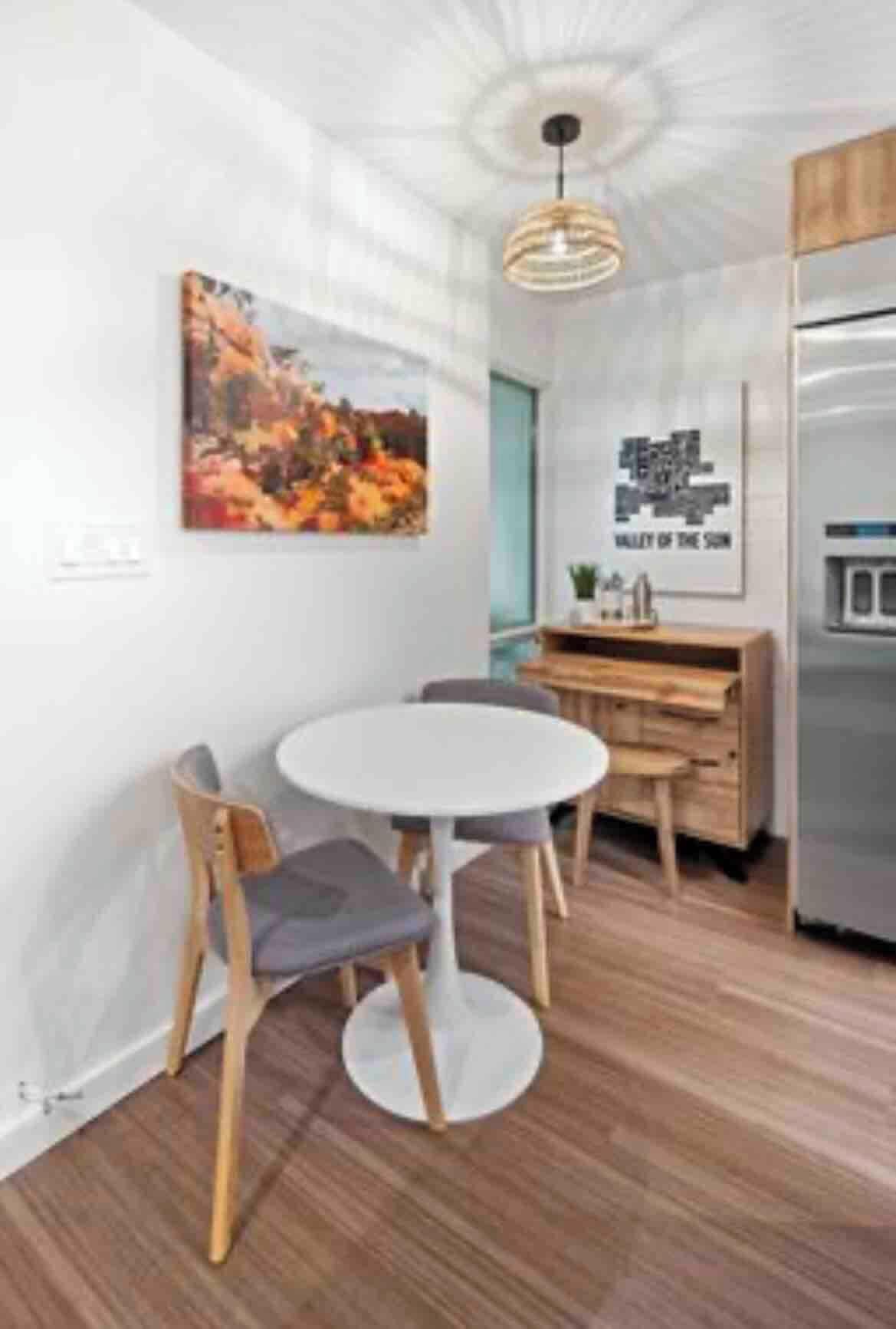 A modern kitchen with a white dining table, wooden chairs, and a hanging pendant light.