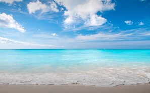 A beach with clear turquoise water and a sandy shore under a bright blue sky with scattered clouds.