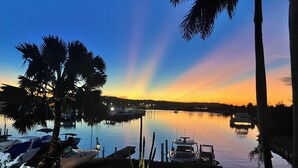 Un puerto deportivo al atardecer con barcos amarrados, palmeras y agua tranquila.