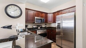 Une cuisine avec des meubles de rangement en bois foncé, un réfrigérateur en acier inoxydable, un four à micro-ondes et une cuisinière.