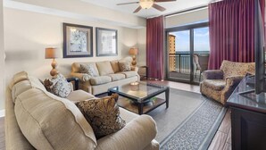 Un salon comprenant un canapé, un fauteuil et une table basse, un ventilateur de plafond et une vue sur l’océan grâce à de grandes fenêtres.