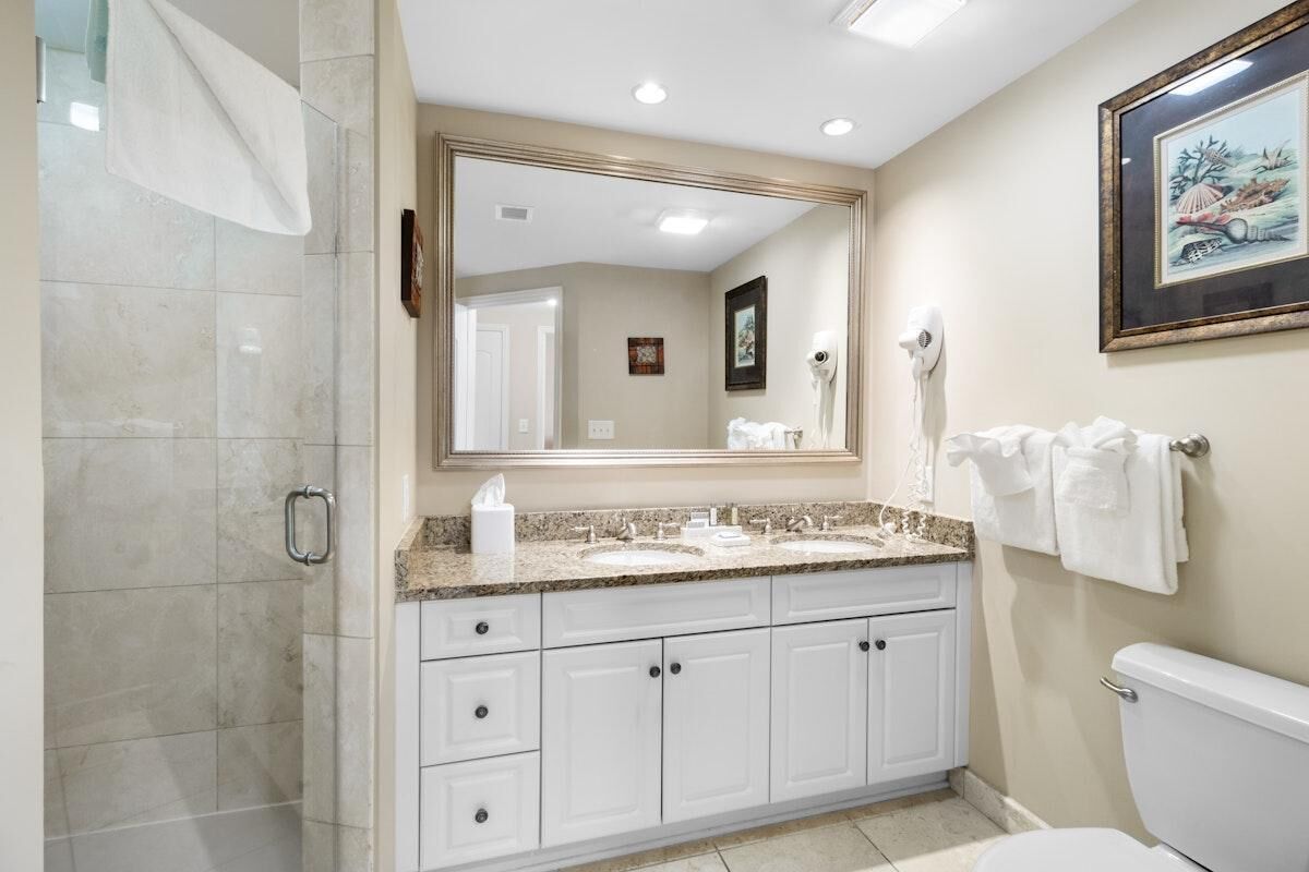 Une salle de bain avec une douche, deux lavabos, des toilettes et un grand miroir.