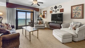A spacious living room with a large TV, comfortable seating, a ceiling fan, and a view to the outside. - Sun Sand Seclusion 2BR Oceanfront Condo Jetted Tub (North Myrtle Beach)