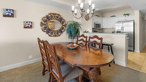 A dining area with a wooden table and chairs, a chandelier, and a kitchen in the background. - Sun Sand Seclusion 2BR Oceanfront Condo Jetted Tub (North Myrtle Beach)