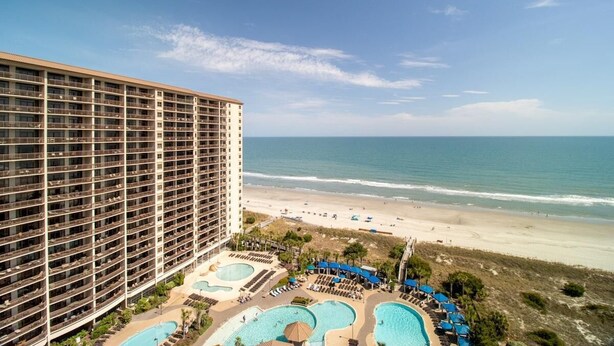 A hotel with multiple floors, a beach view, and a pool area with umbrellas. - Sun Sand Seclusion 2BR Oceanfront Condo Jetted Tub (North Myrtle Beach)