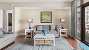 A living room with a grey sofa, a white coffee table with baskets, two side tables with lamps, and a ceiling fan. - Beachfront Elegance: 2BR Condo with Jetted Tub (North Myrtle Beach)