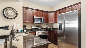A kitchen with wooden cabinets, a stainless steel refrigerator, a microwave, a stove, and a sink. - Beachfront Elegance: 2BR Condo with Jetted Tub (North Myrtle Beach)