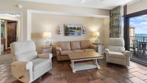 A living room with a beige sofa, two armchairs, a coffee table, and a ceiling fan. There are two wall-mounted lamps and a painting above the sofa. - Spacious Coastal Comfort 2BR Condo with Balcony (North Myrtle Beach)