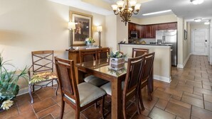 A dining area with a wooden table and chairs, a chandelier, and a kitchen in the background. - Spacious Coastal Comfort 2BR Condo with Balcony (North Myrtle Beach)