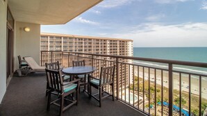 A balcony with a table and chairs, overlooking a beach and a hotel building. - Spacious Coastal Comfort 2BR Condo with Balcony (North Myrtle Beach)