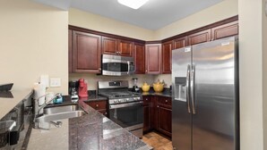 A kitchen with dark wooden cabinets, stainless steel appliances including a microwave, stove, oven, and refrigerator. - Spacious Coastal Comfort 2BR Condo with Balcony (North Myrtle Beach)