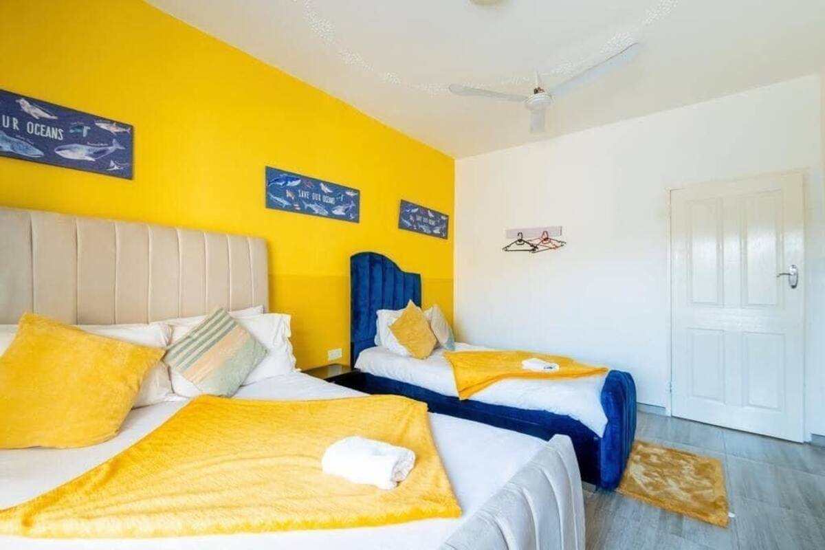 Ein Hotelzimmer mit zwei Betten, gelber Bettwäsche, einem weißen Deckenventilator und einer Tür.