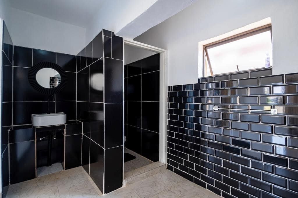 A modern bathroom with black tiled walls, a round mirror, and a window.
