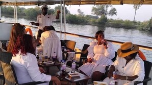 A group of people seated on a boat with a view of a river and trees. - The Crescent Victoria Falls  (Victoria Falls)