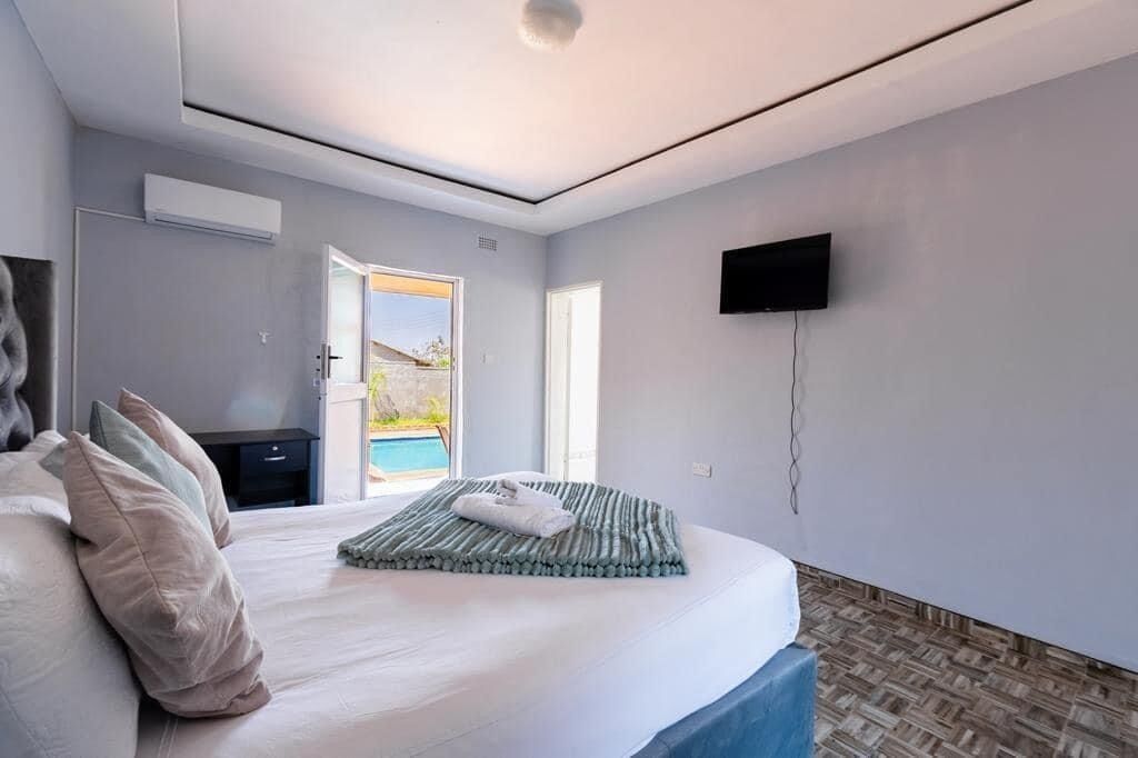 Un dormitorio con una cama grande, un televisor de pantalla plana montado en la pared y vista a una piscina a través de una puerta abierta.