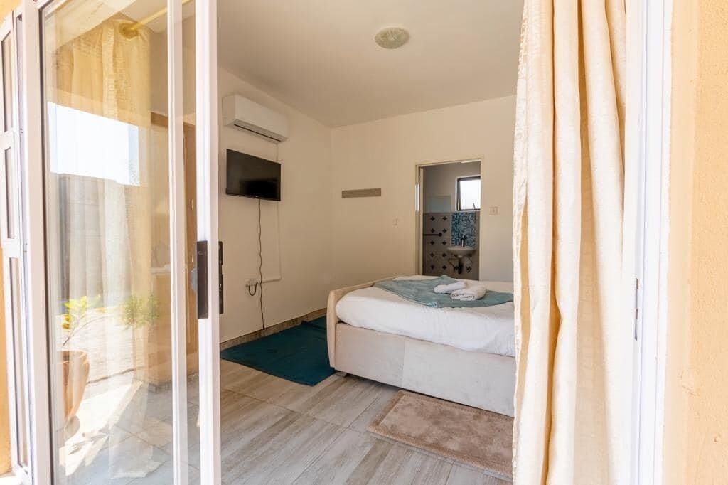 A bedroom with a bed, a TV mounted on the wall, and a sliding glass door leading to a balcony.