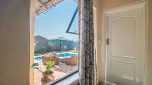 A room with a view of a swimming pool, wicker furniture, and a closed door. - The Crescent Victoria Falls  (Victoria Falls)
