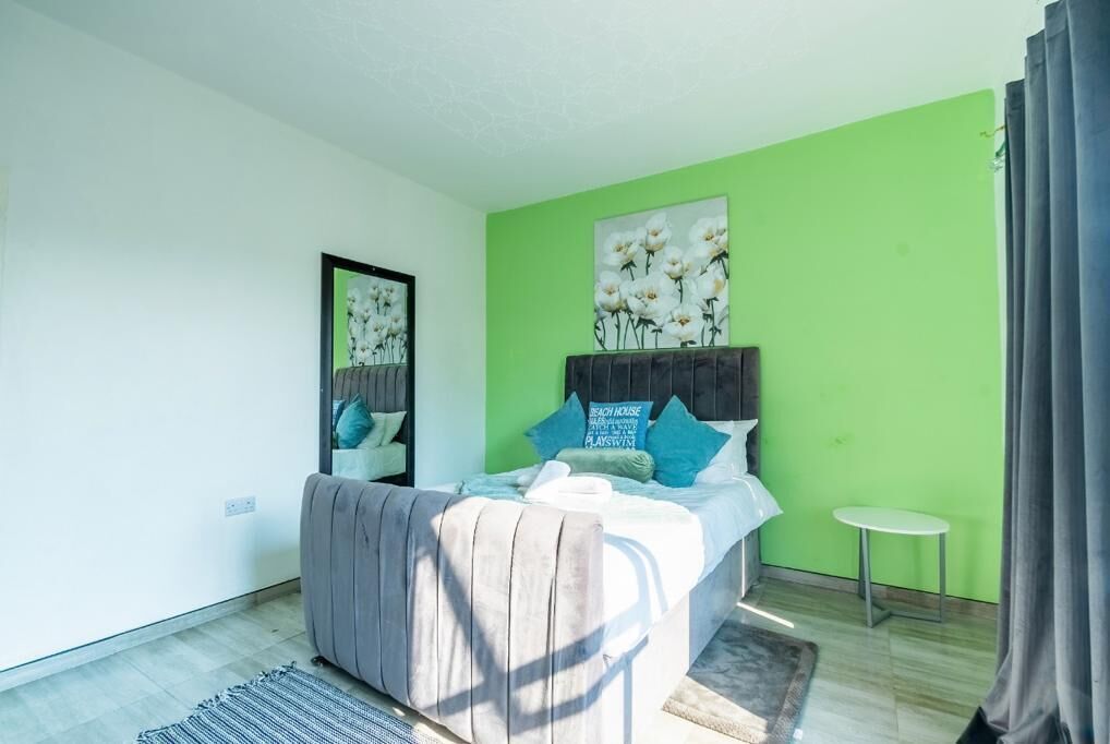 A bedroom with a bed, a small round table, and a green accent wall.