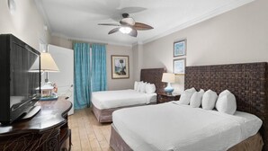 A hotel room with two beds, a TV, a ceiling fan, and a dresser.