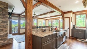 A spacious kitchen with dark cabinetry, a large island, and a stone accent wall. - Chalakee Lodge CF-2- Mountain View, Gated Resort, Indoor/Outdoor Pools & Hot Tub (Boone)