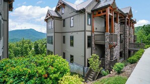 A multi-story building with a stone facade, wooden balconies, and a view of a mountainous landscape. - Chalakee Lodge CF-2- Mountain View, Gated Resort, Indoor/Outdoor Pools & Hot Tub (Boone)