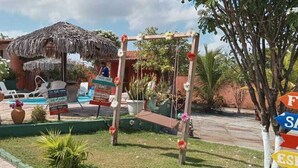 Un espace piscine équipé de chaises longues, d’une structure à toit de chaume et de panneaux indiquant les équipements disponibles.