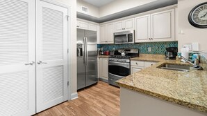 A modern kitchen with white cabinets, stainless steel appliances, a granite countertop, and a clock on the wall.