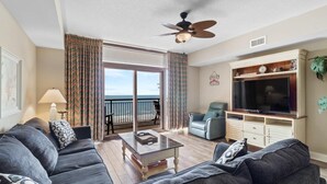 A living room with a sofa, a coffee table, a TV, and a balcony with curtains.